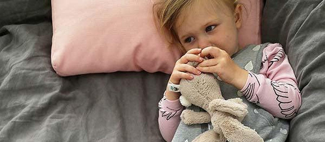 Toddler in striped merino pyjamas sitting on a bed